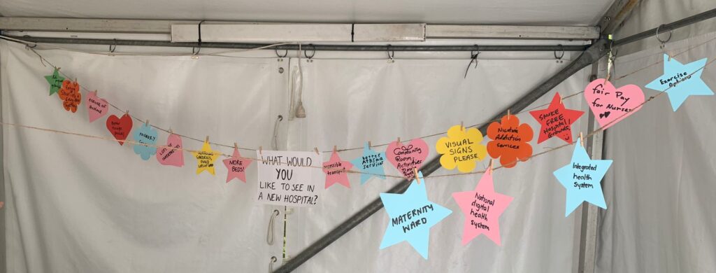 Bunting (paper decorations in a row on a string) have been made out of paper stars, hearts, and flowers. They are pink, orange, yellow, green, red, and blue. Each has an answer written on it, and in the middle is the questions "What would YOU like to see in a new hospital?"