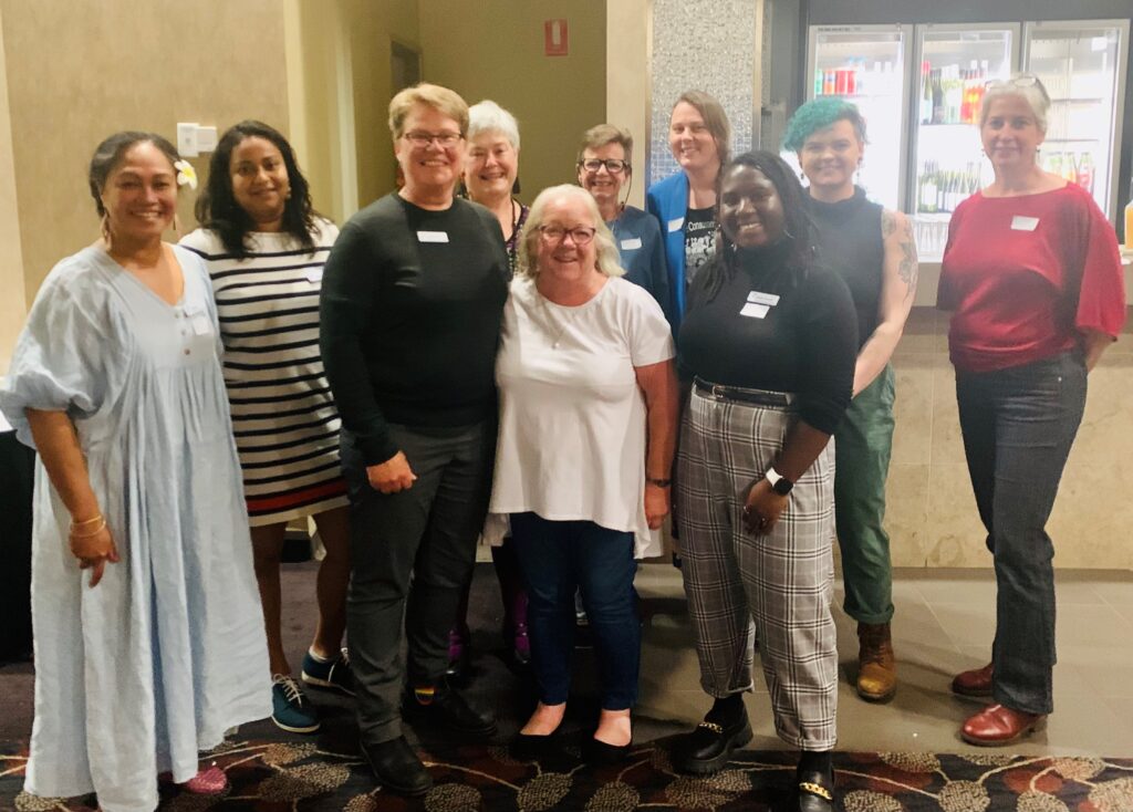 A smiling group of people of varying ages and races stand in a lobby facing the camera. It's the HCCA gang – seven staff and three members.